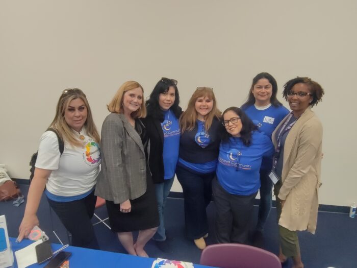 Seven women smile at the camera standing in a conference room.